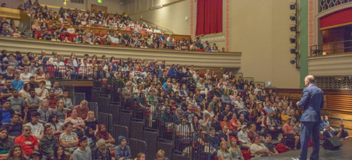 A man giving a talk to a packed theatre