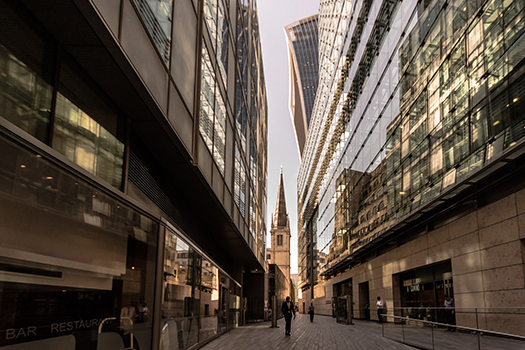 Photo taken at sunrise between two office buildings in the City of London with a church spire in the background