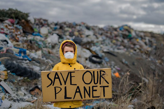 A person holding a sign saying 'save our planet' in a dump full of rubbish