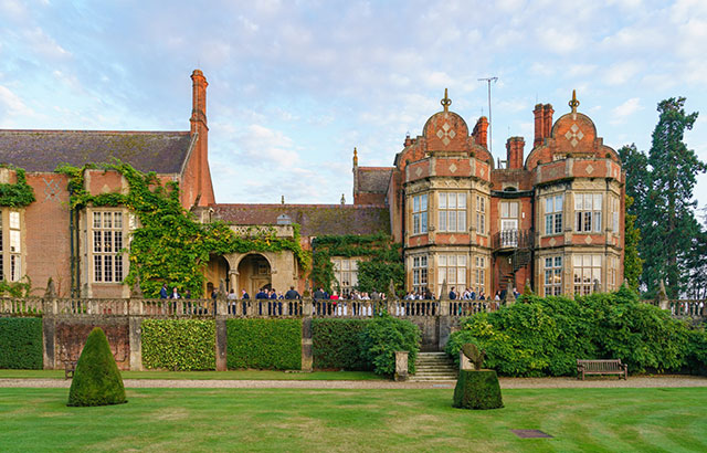 The outside of Tylney Hall. It is a red bricked manor house with wisteria growing up the walls.