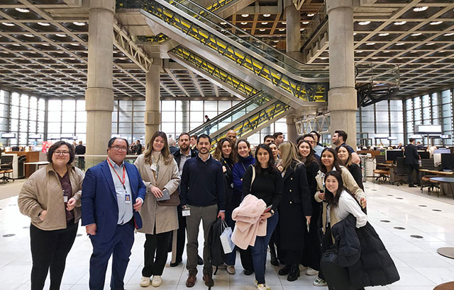 Queen Mary Insurance Law LLM students inside Lloyd's of London. Is is a multi-story office space with central escalators lit in yellow.