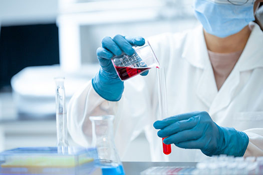 A medical tester wearing PPE pouring liquid between test tubes