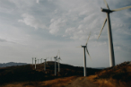 A hilly landscape with a row of wind turbines against a cloudy sky