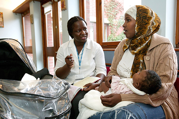 A woman sitting with her baby on her lap talks to a healthcare professional in a GP practice