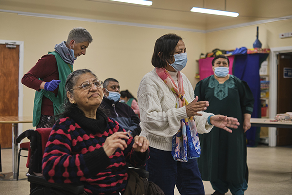 Image shows a group of five people, seated and standing, taking part in an activity in a community centre.