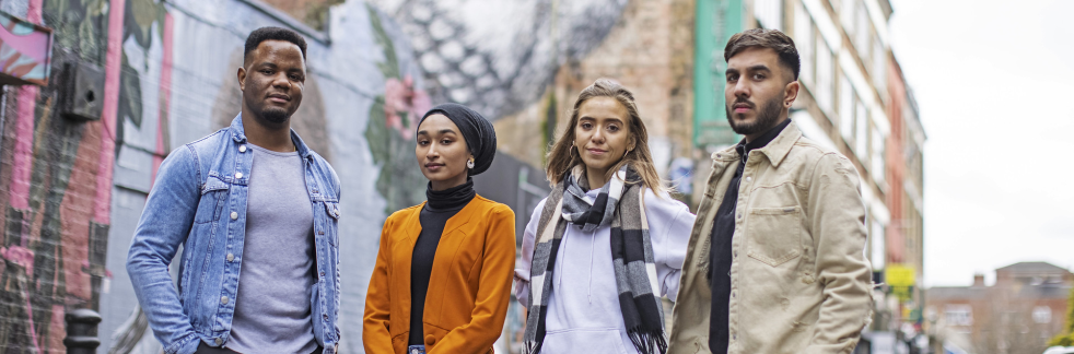 A group of four students standing in front of street art depicting a bird in London