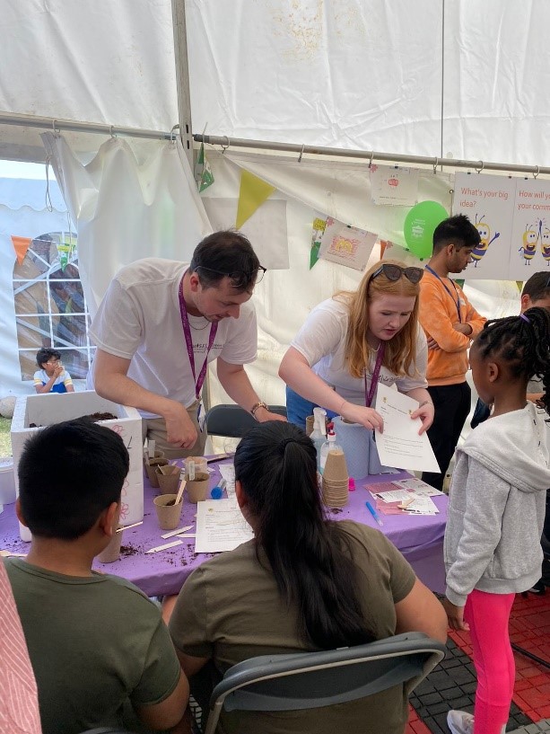 WISE stall staff during the 2022 Festival of Communities giving instructions for the Plant your own Sunflower seeds activity