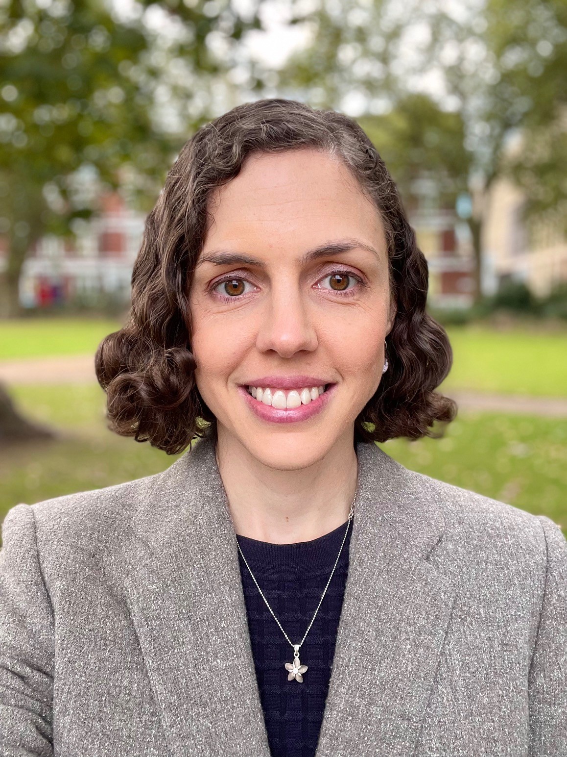 Kate Goddard image in grey jacket with black top with trees and lawn behind