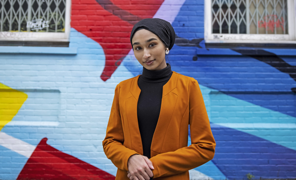 Female student standing in front of a mural in East End