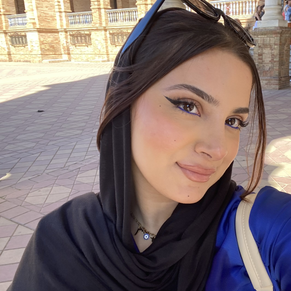 Headshot of alumna, Shamem Faizi. She is loosely wearing a black headscarf so that the front of her hair is showing and she has sunglasses on her head.