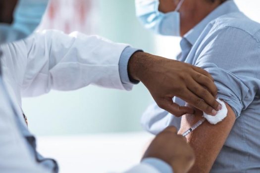 A man wearing a face mask is injected in his left arm with a hypodermic needle