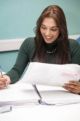 A smiling woman writing in a notepad, holding a highlighted document