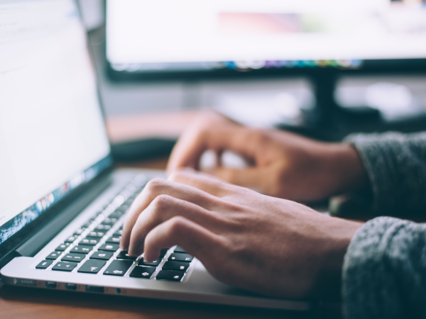 A photograph of two hands typing at a laptop