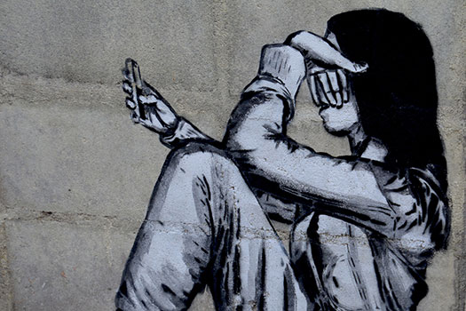 Graffiti on a wall of a girl looking sad using a phone