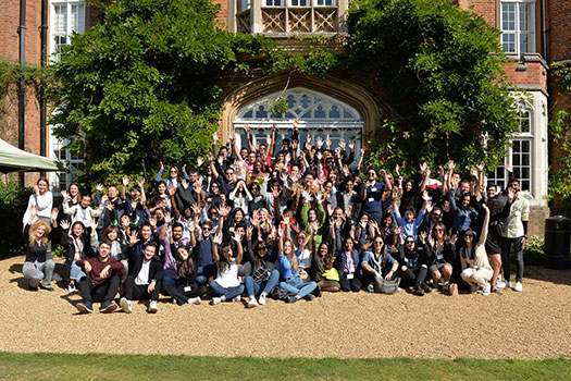 A group photo of Queen Mary Postgraduate Law Students outside Cumberland Lodge. The group is framed by foliage growing around the building.