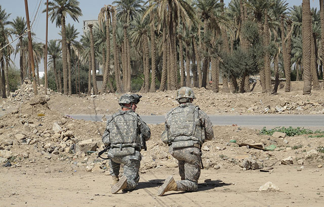 Two soldiers kneeling on the side of the road in Iraq.