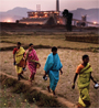 Four Indian women walking along a a field by a factory