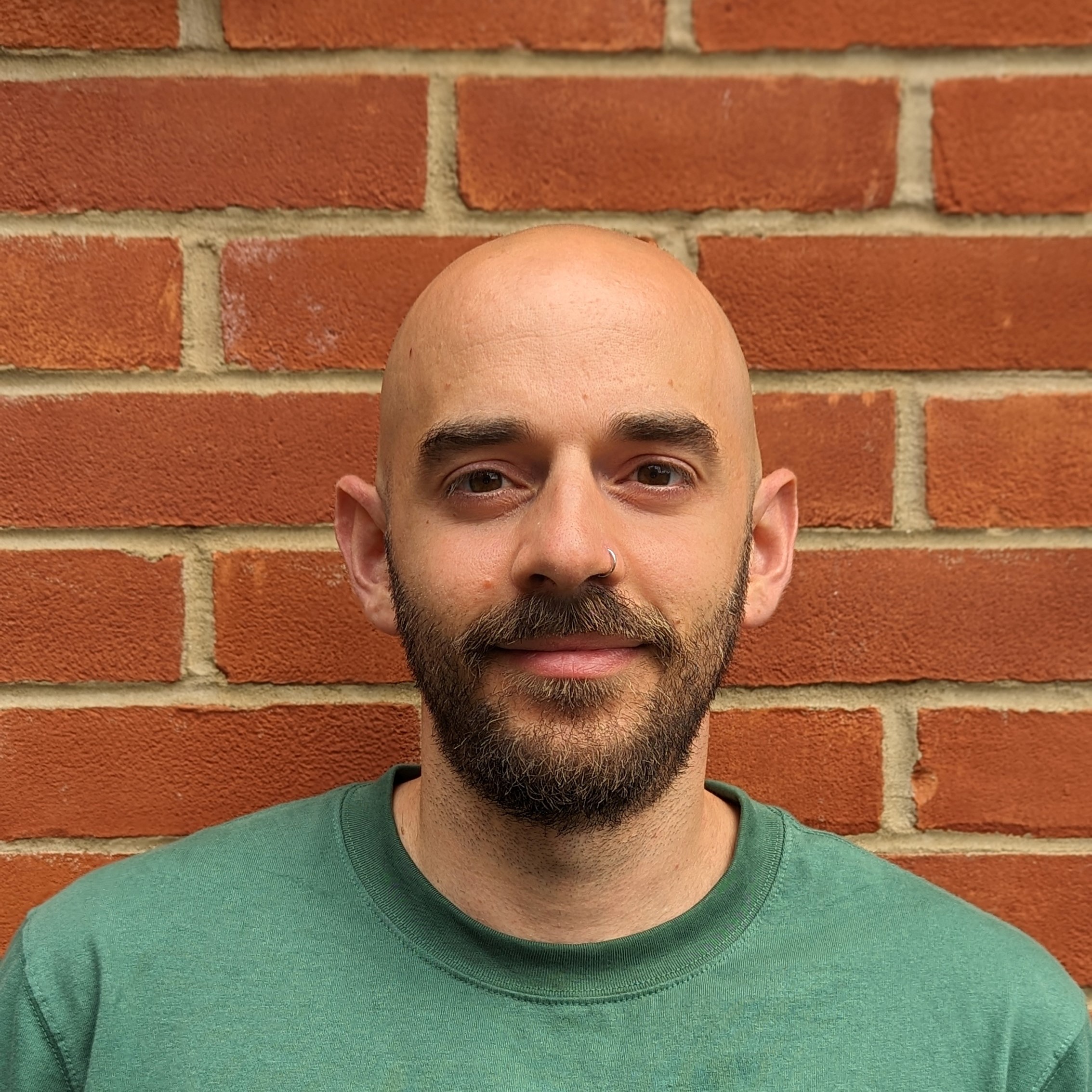 Dr Nikos Bempedelis wearing a green sweatshirt, standing in front of a brick wall