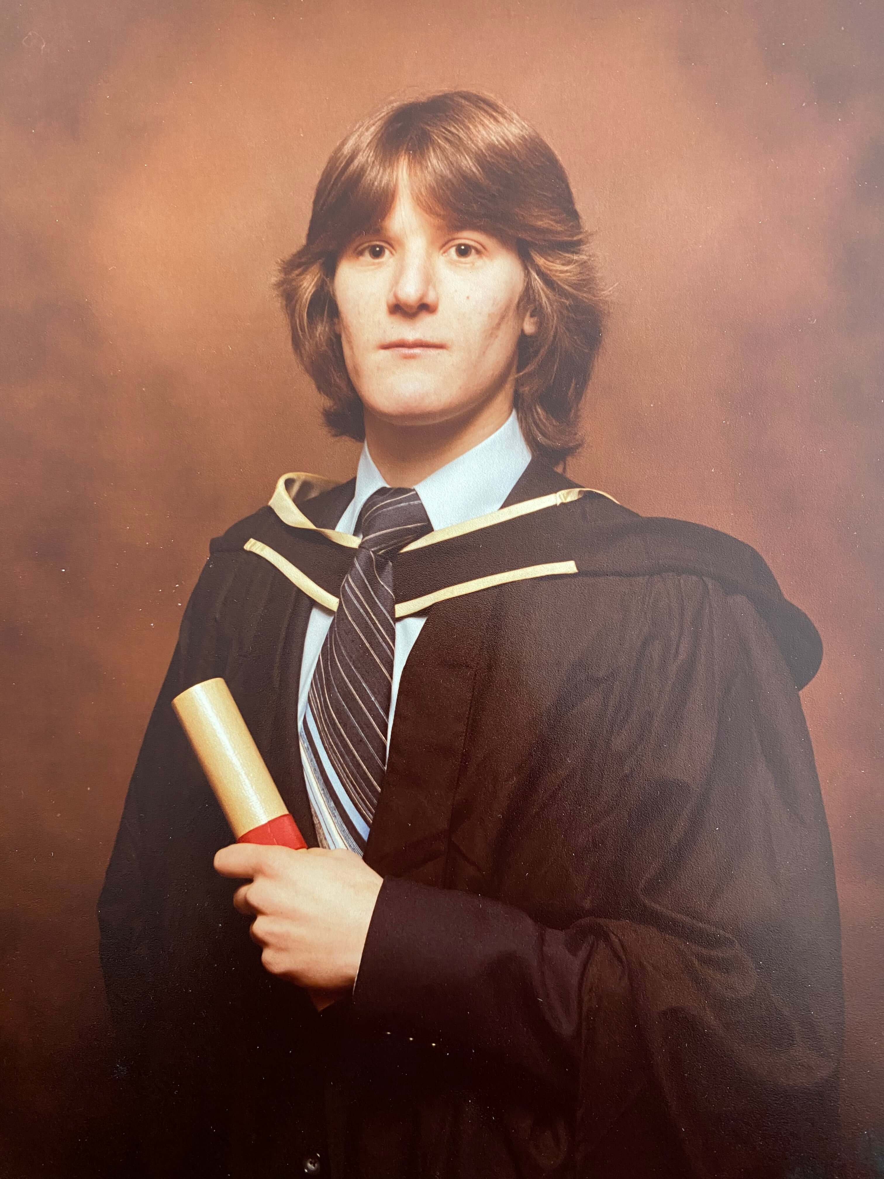 Trevor Witton at graduation; holding a scroll and cloaked in a gown.