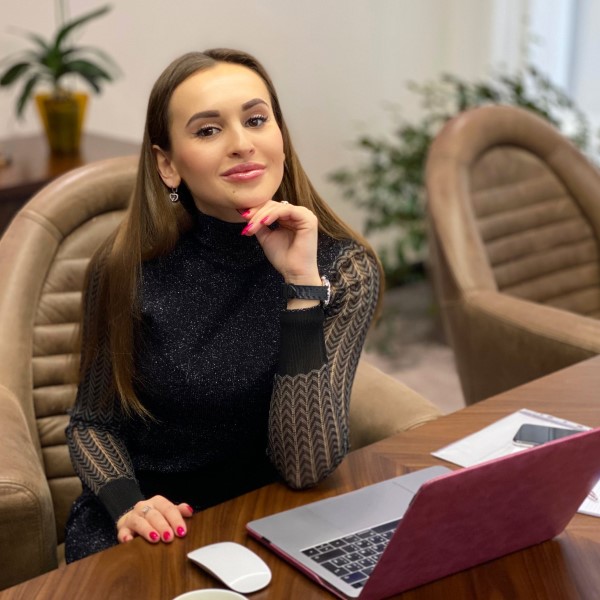 Photo of alumna, Vasylisa Bondarenko. She is sat at a table in front of a laptop with her chin resting on her hand.