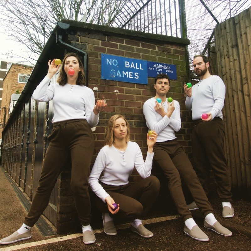 Photo of comedy collective, Zazu. The four members are wearing white tops and brown trousers and each holding two balls in front of a 