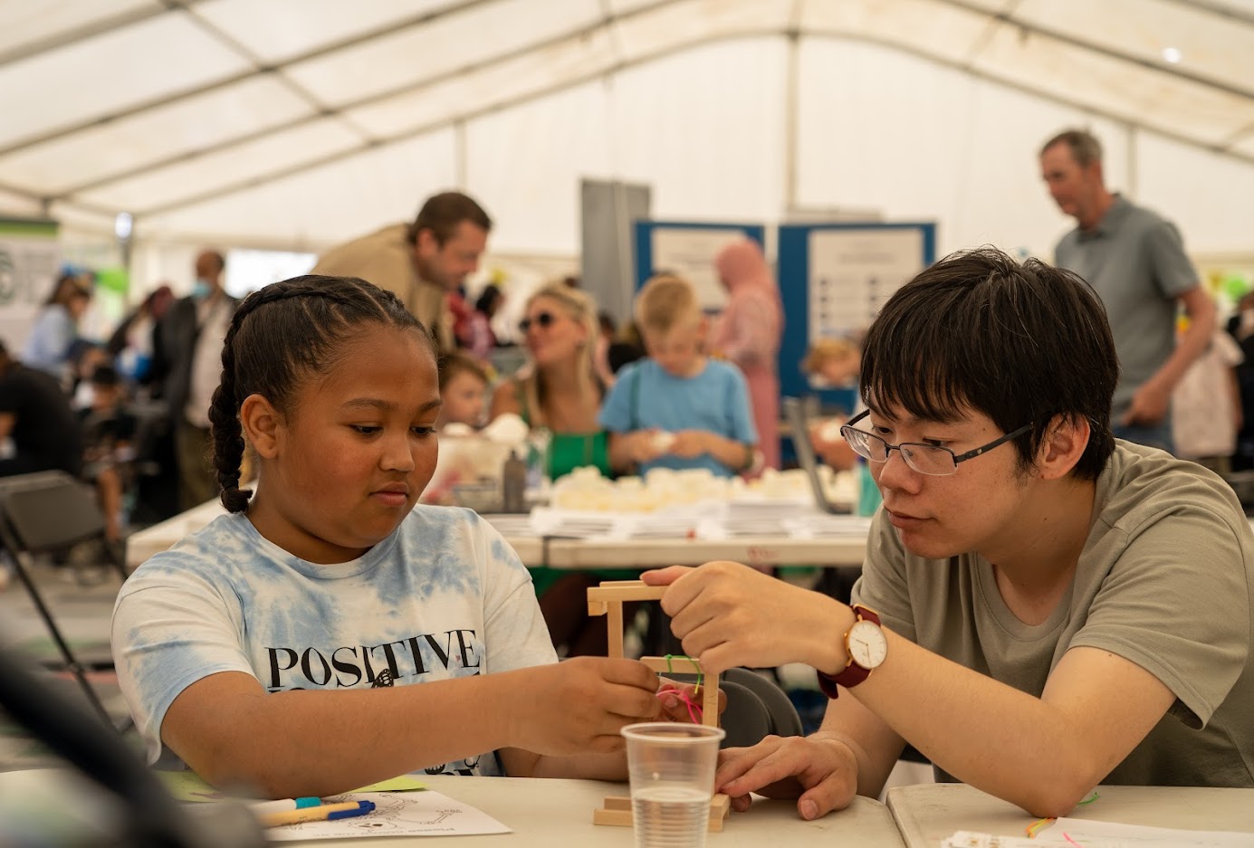 A researcher shows a girl how to build a wooden structure at the Festival of Communities