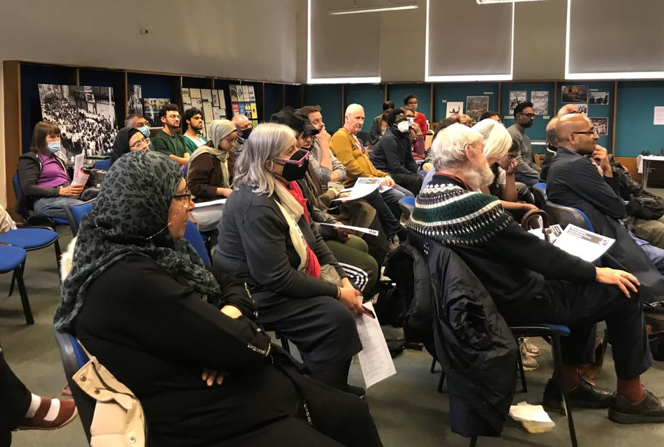 A group of people listening to talks in front of an exhibition of anti-racist activist material from the 1970s