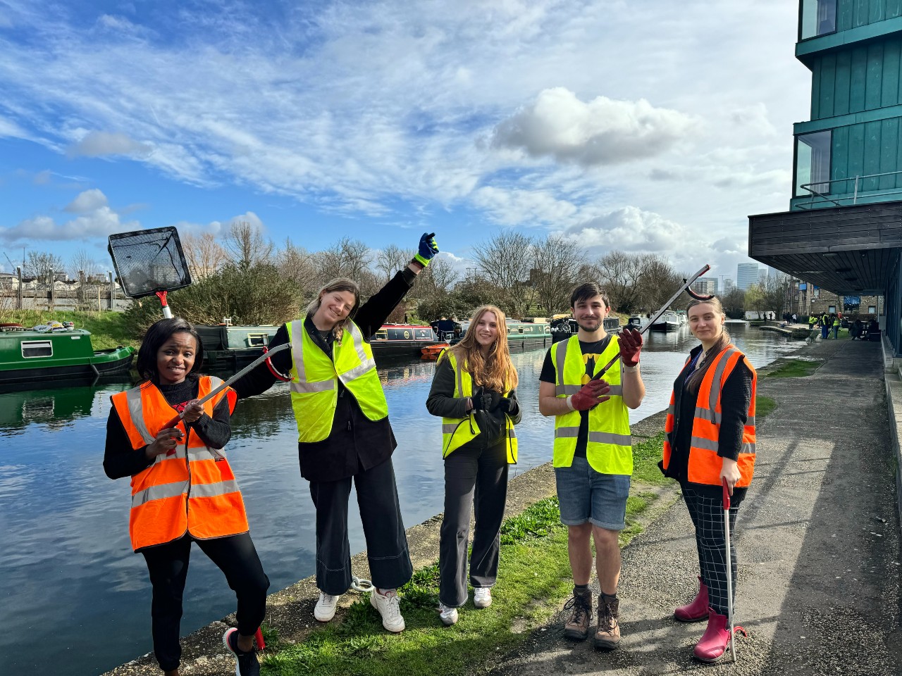 A group of five students with litter pickers and nets posing next to Regent's Canal on the Mile End Campus after cleaning the canal as part of Climate Action Week.