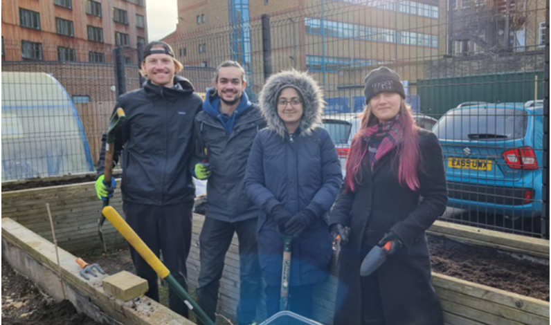 Students smiling next to the raised beds allotments after doing some gardening.