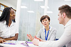 A black woman, a white woman and a white man sat in a meeting room having a discussion