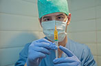 Male nurse wearing a medical mask, scrubs and cap holding a syringe