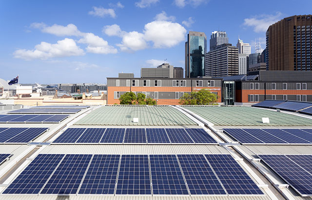 Solar panels on the roof of a building with skyscrapers in the background.