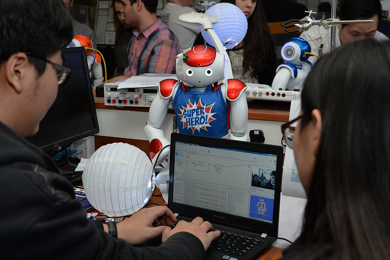 Students sit by a computer and a robot