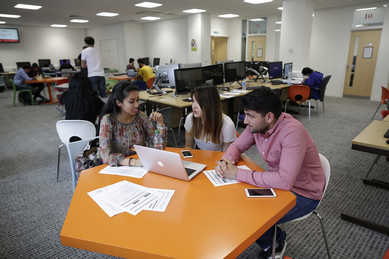 A small group of students work together on laptop and paper