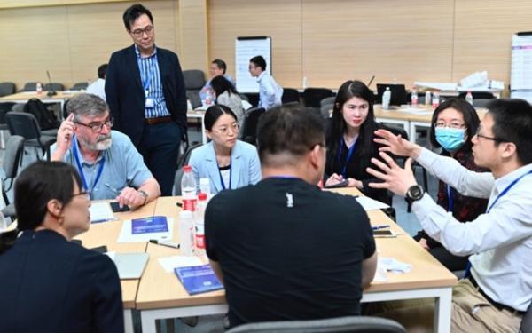 Students and educators in group discussion around tables in a large room