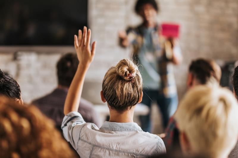 Students in a classroom, one has her hand raised