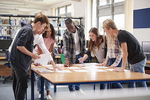 Seven students standing round a table looking down