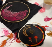 Embroidered hoops with a black backgrounds. One has a pink landscape and one has a moon and sun and some flowers stitched on.