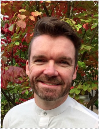 Portrait photograph of Dylan Glyn Williams standing in front of a tree and smiling.