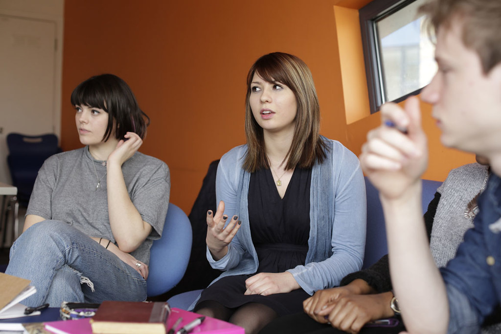 Three students talking in a room with orange walls