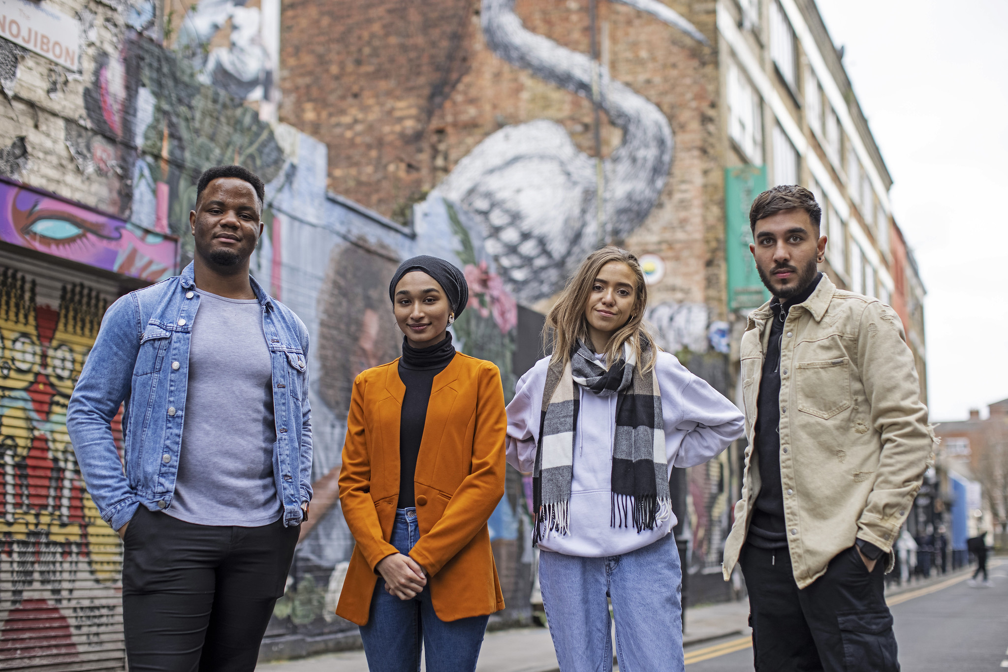 Four students posing in front of buildings with graffiti