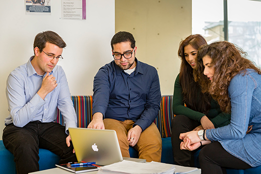 Four people sitting and discussing in front of a laptop