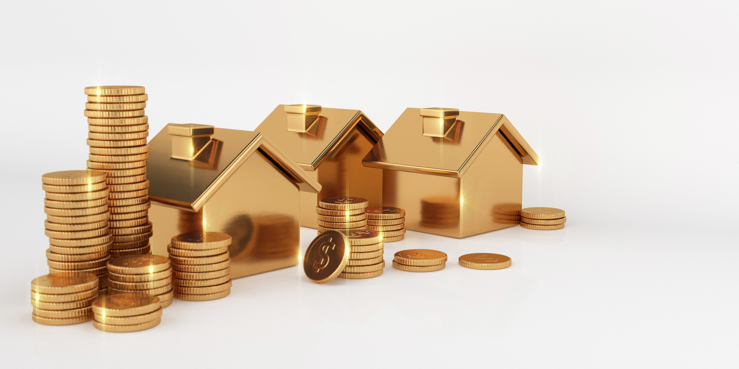 Miniature, golden models of houses and coins on a white surface