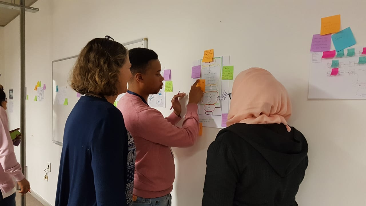 Two women and a man work together on a public advisory consultation, using sticky notes to make comments on a plan displayed on a wall.