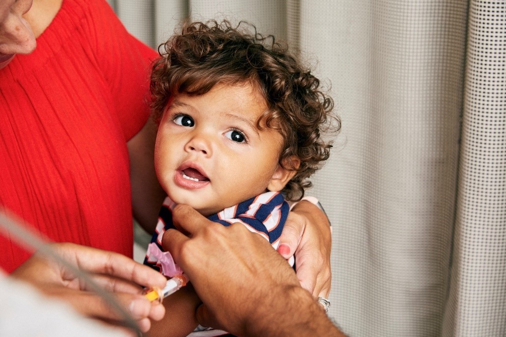 A toddler sits on his mother's lap, whilst receiving a vaccination in his arm.